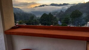 A balcony with two wooden stools and a view of a mountainous landscape. - Hostal De María (San Cristóbal de las Casas)