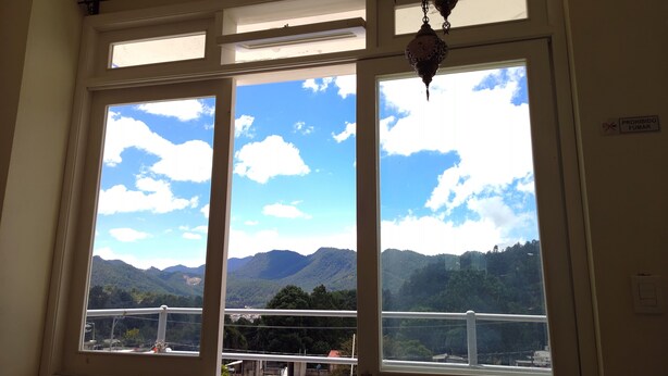 A room with a large window offering a view of mountains and a clear sky. - Hostal De María (San Cristóbal de las Casas)