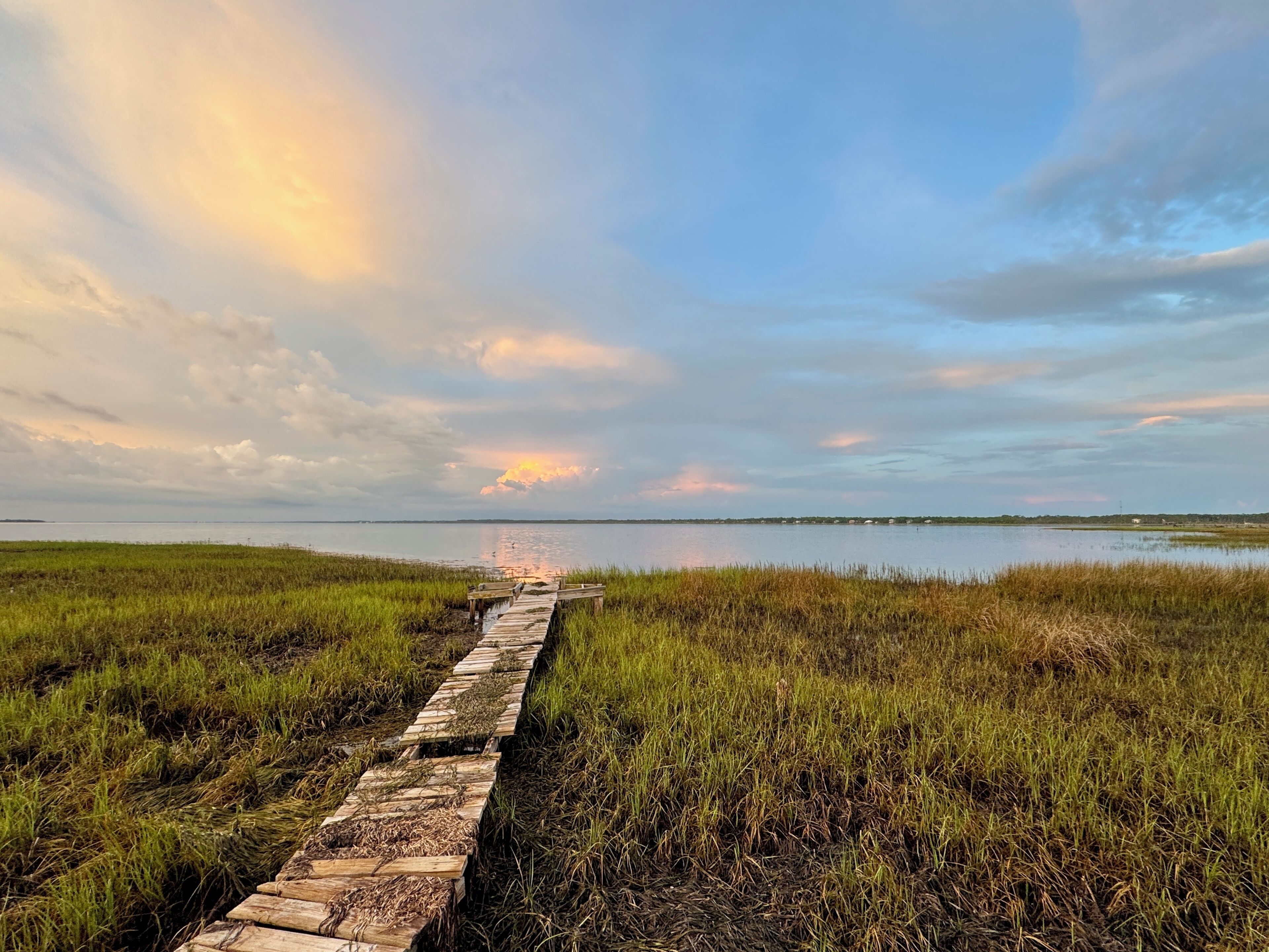 A wooden boardwalk leading to a body of water with a sunset in the background.