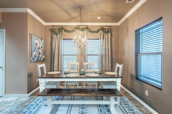 Un comedor con una mesa de madera, cuatro sillas, una araña y una ventana con persianas.