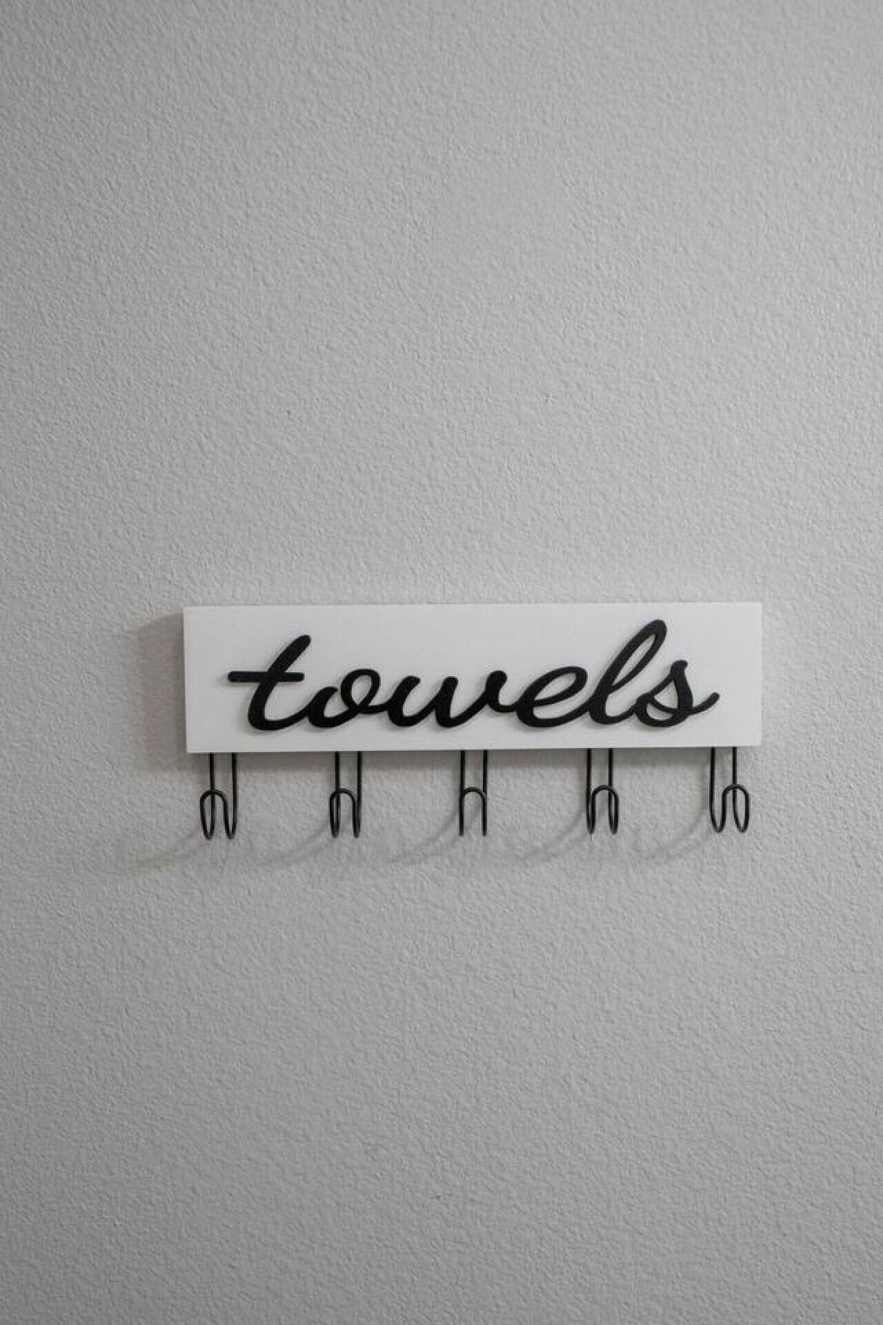 Un toallero de pared con la palabra 'towels' en cursiva sobre un fondo blanco.