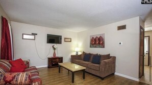 A living room with a sofa, a coffee table, a TV, and a painting on the wall. - Cozy 2-bedroom townhome in awesome Columbia with AC. (Columbia)