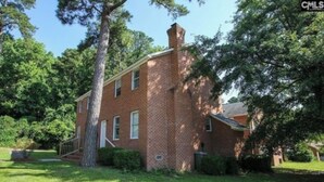 A brick building with a chimney, surrounded by trees and a well-maintained lawn. - Cozy 2-bedroom townhome in awesome Columbia with AC. (Columbia)