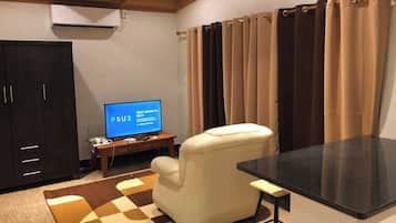 Un salon avec un téléviseur à écran plat affichant un message d’erreur concernant la connexion Wi-Fi, un fauteuil beige, une petite table d’appoint en bois et un tapis à carreaux.