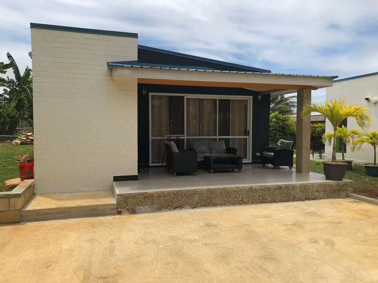 Une maison moderne dotée d’un patio comprenant un canapé et des fauteuils, un espace salon couvert et un mur en pierre.