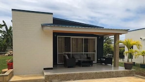A modern house with a patio area featuring a sofa and chairs, a covered seating area, and a stone wall. - Elite Island Staying (Nuku'alofa)