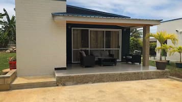 Une maison moderne dotée d’un patio comprenant un canapé et des fauteuils, un espace salon couvert et un mur en pierre.