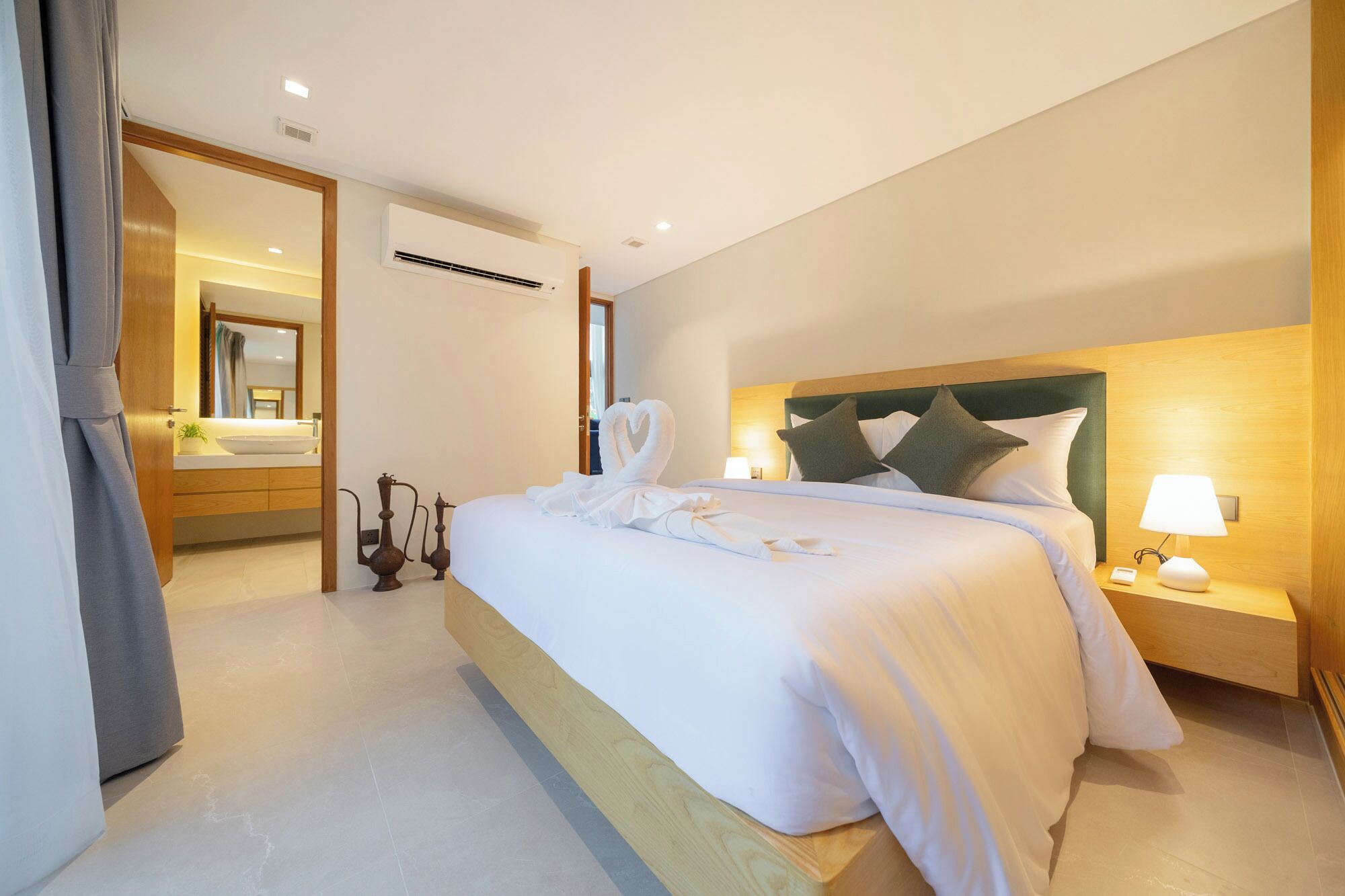 A hotel room with a large bed, bedside lamps, a wooden headboard, and a bathroom visible through an open door.
