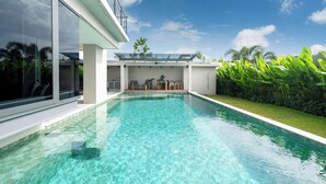 Ein moderner Poolbereich mit klarem Wasser, einer überdachten Terrasse aus Glas und üppiger Bepflanzung.