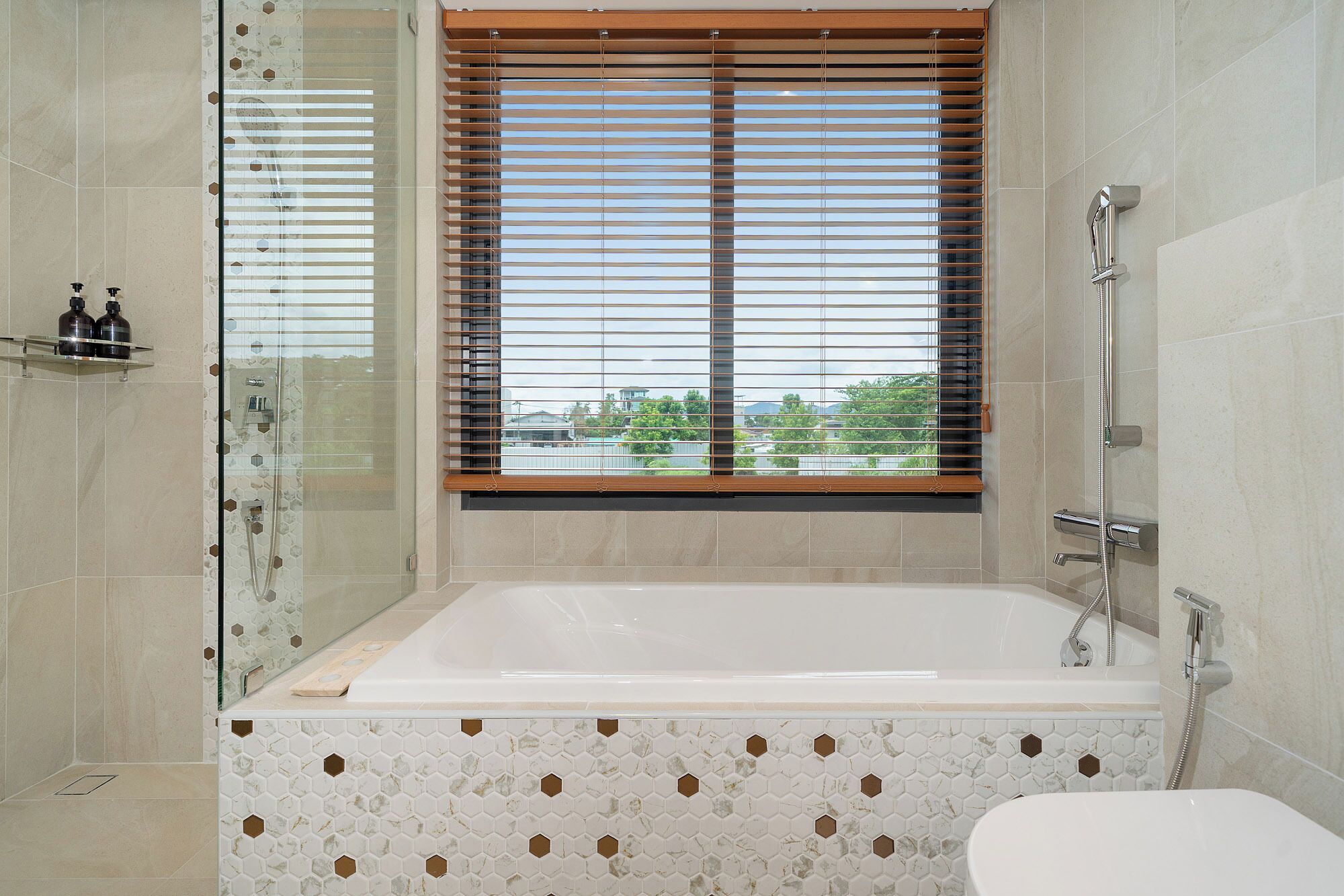A bathroom with a bathtub, shower, and a window with blinds.