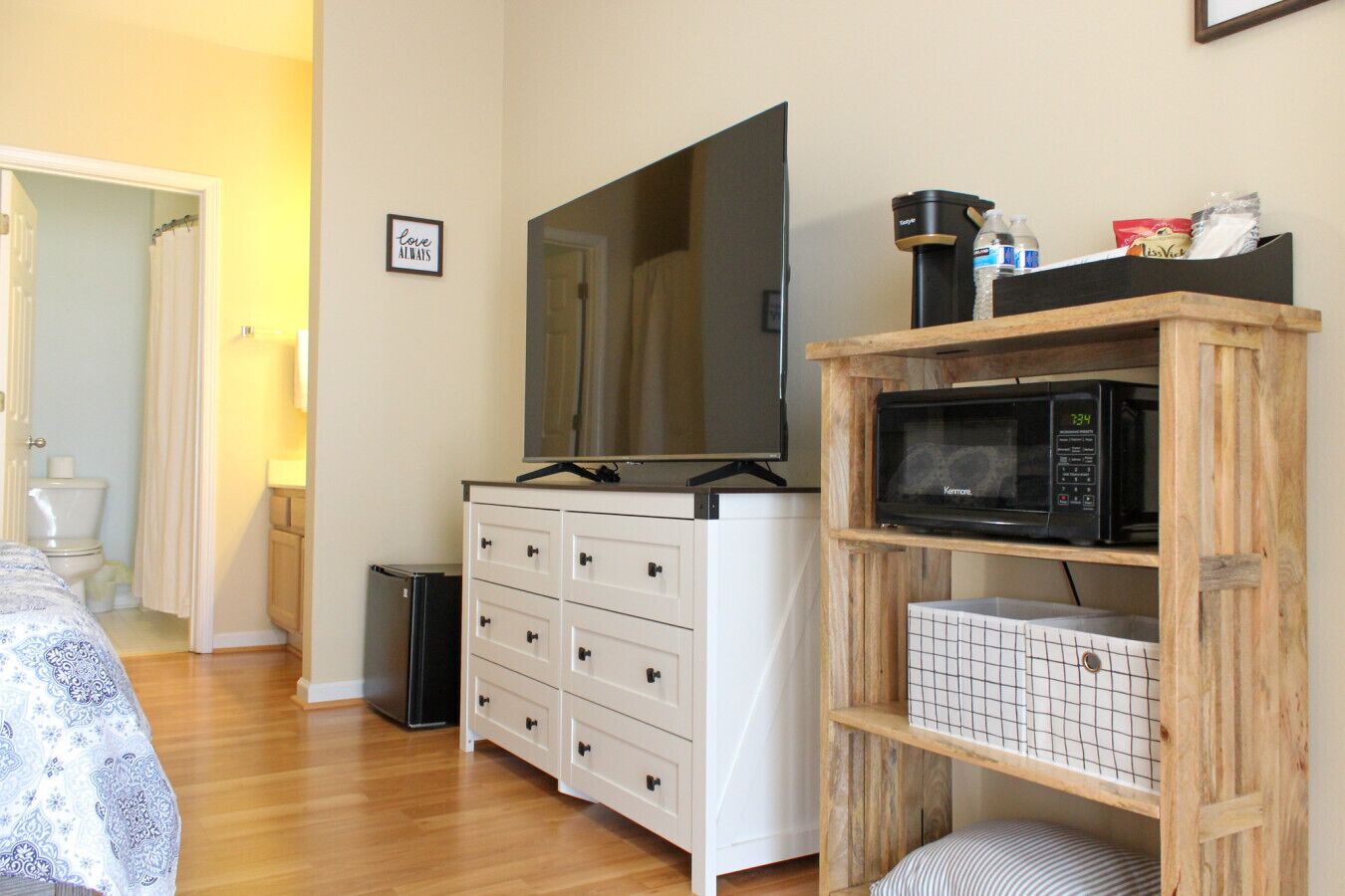 Un dormitorio con un aparador blanco, un espejo grande, un televisor, un microondas y un mueble pequeño.