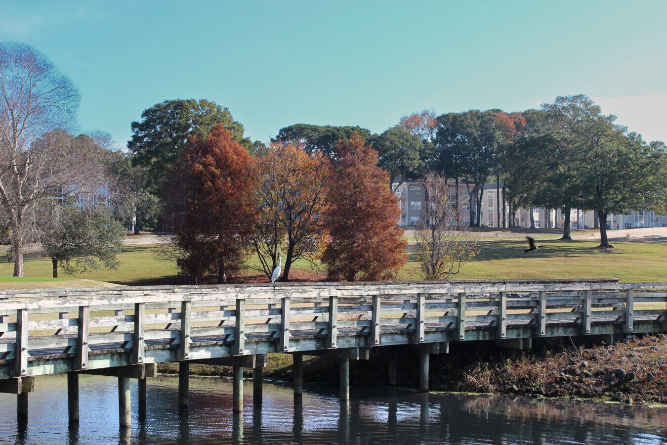 A wooden bridge over a body of water with trees and a building in the background.