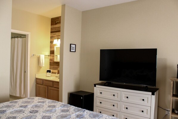 Une chambre d’hôtel avec un lit, un téléviseur posé sur une commode, une salle de bain avec un rideau de douche et un mur décoratif en bois.