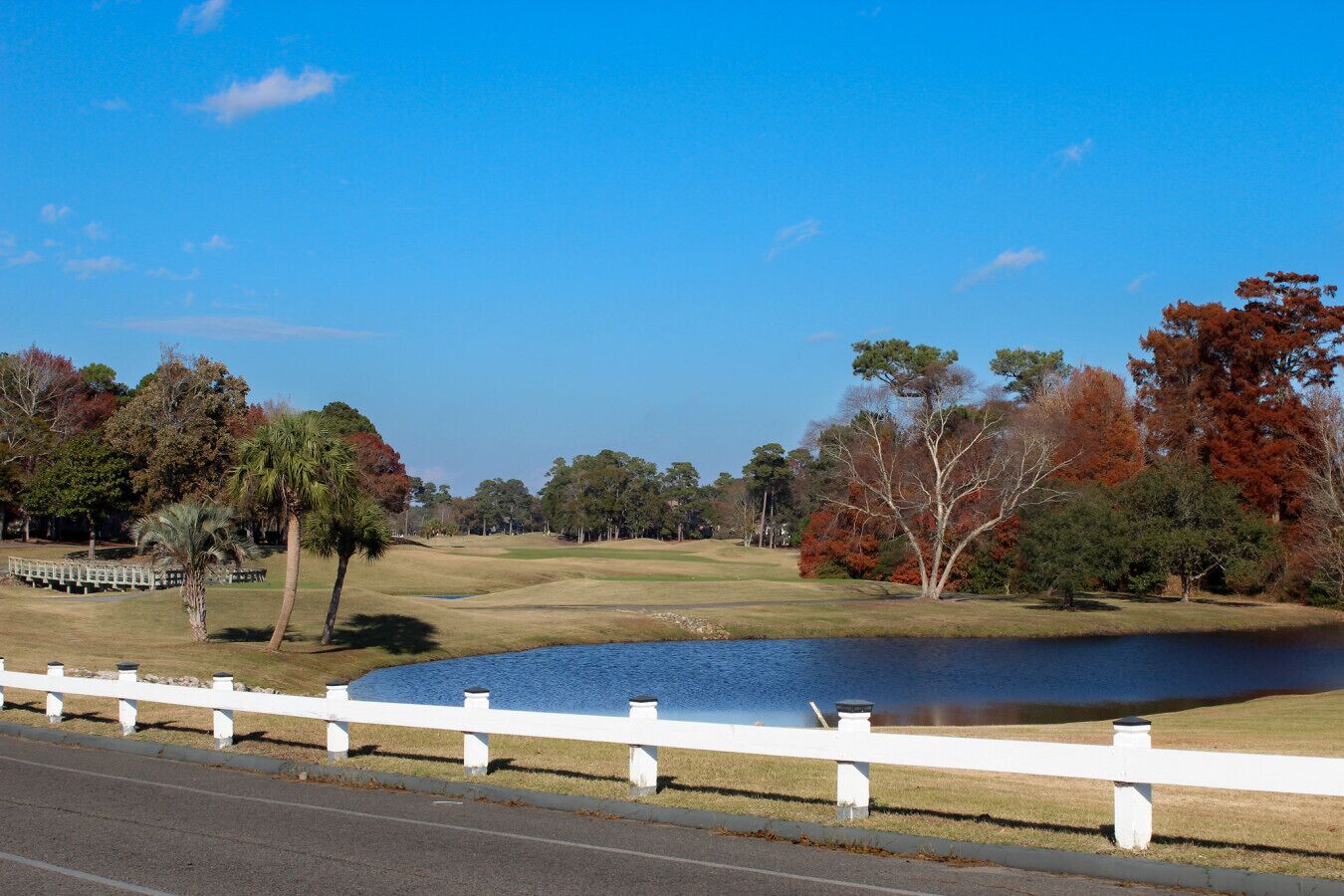A golf course with a pond, white fence, and autumn trees.