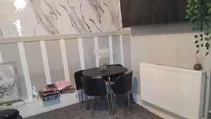 A room with a marble-patterned wall, a black dining table with four chairs, a white radiator, and a potted plant. - Modern Seaside Stay at Bela Grove-Sleeps8 (Blackpool)