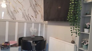 A modern room with a marble wall, a round table with chairs, a white radiator, and shelves with plants. - Modern Seaside Stay at Bela Grove-Sleeps8 (Blackpool)
