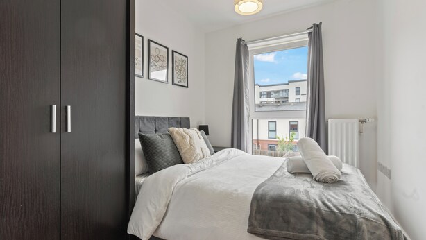 A bedroom with a bed, dark wooden wardrobe, and a window with curtains.