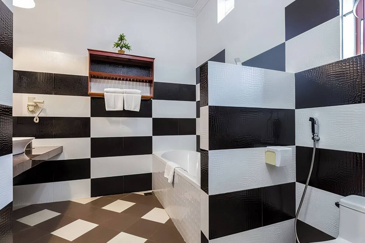 A bathroom with black and white checkered tiles, a bathtub, a shower, a sink, and a small shelf with a plant.