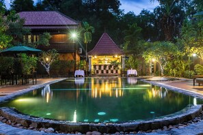 A pool area with a bar and seating, surrounded by lush greenery and a building with a red roof. - De Arya Angkor Resort (Siem Reap)