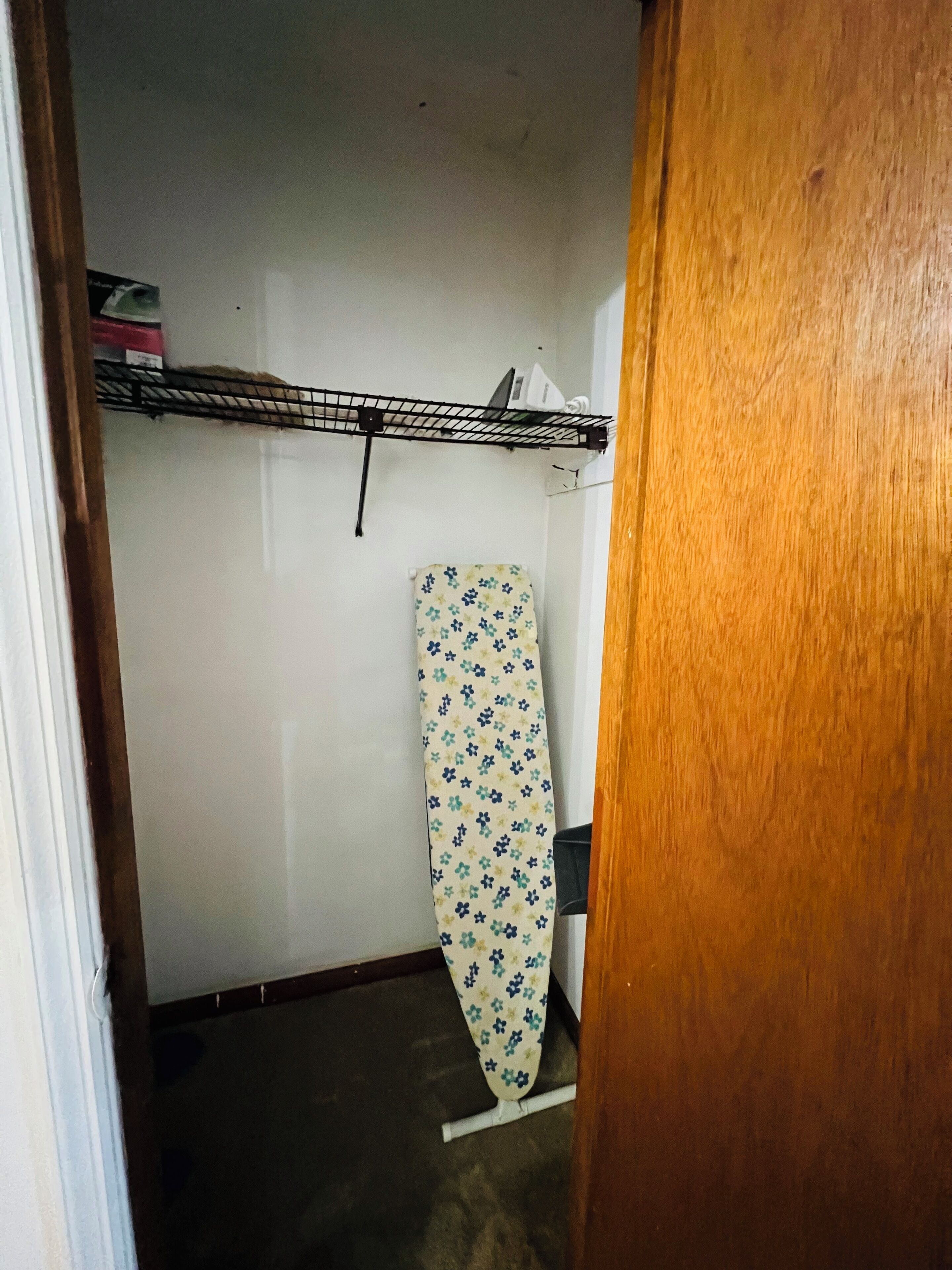 Een kamer met een houten deur, een metalen plank met een doos, en een gestreept strijkplank.