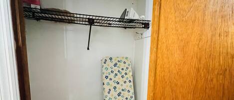Een kamer met een houten deur, een metalen plank met een doos, en een gestreept strijkplank.