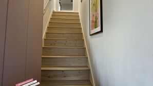 Een houten trap die leidt naar een kamer met witte wanden en een ingelijst kunstwerk.