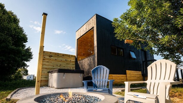 Un espace de détente extérieur moderne, doté d’un foyer, de deux fauteuils Adirondack et d’une terrasse en bois.