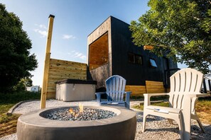 Un espace de détente extérieur moderne, doté d’un foyer, de deux fauteuils Adirondack et d’une terrasse en bois.