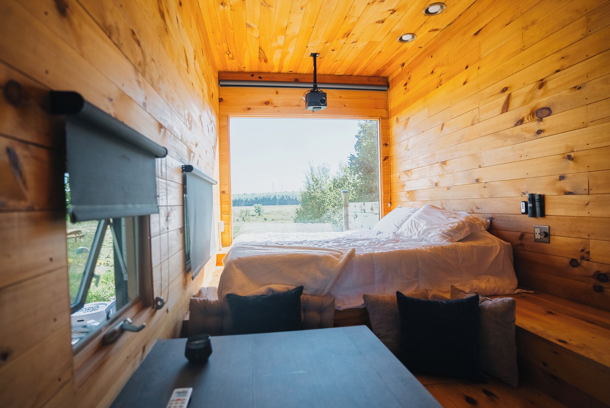 A wooden cabin room with a bed, a table, and a window.