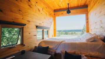 A wooden cabin bedroom with a bed, a table, and a window.