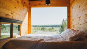 Une chambre dans une cabane en bois, avec un lit, un projecteur et une grande fenêtre donnant sur un paysage.