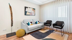 A modern living room with a grey sofa, two black chairs, a yellow pouf, and a large abstract painting on the wall. - GuestReady - Lovely Urban Retreat (Porto)