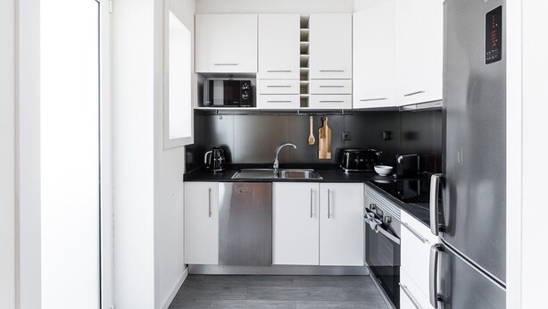 A compact kitchen with white cabinets, a black countertop, stainless steel appliances, and a black oven. - GuestReady - Lovely Urban Retreat (Porto)