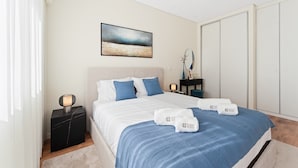 A modern bedroom with a bed, bedside tables, a nightstand, a painting, and a wardrobe. - GuestReady - Lovely Urban Retreat (Porto)