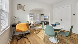 A modern living room with a dining area, wooden flooring, and a TV mounted on the wall. - Pet-Friendly 1BR Duplex Near Butler University ~ Sleeps 2 ~ Fast Wi-Fi (Indianapolis)