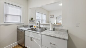 A modern kitchen with a dishwasher, sink, and a countertop with a paper towel dispenser. - Pet-Friendly 1BR Duplex Near Butler University ~ Sleeps 2 ~ Fast Wi-Fi (Indianapolis)