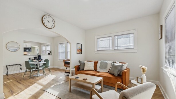 A modern living room with a sofa, coffee table, and chairs. There is a dining area with a table and chairs. A clock is visible on the wall. - Pet-Friendly 1BR Duplex Near Butler University ~ Sleeps 2 ~ Fast Wi-Fi (Indianapolis)