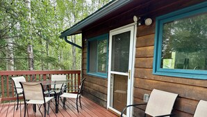 Une cabane en bois dotée d’une terrasse, d’une porte vitrée et d’une table avec des chaises.