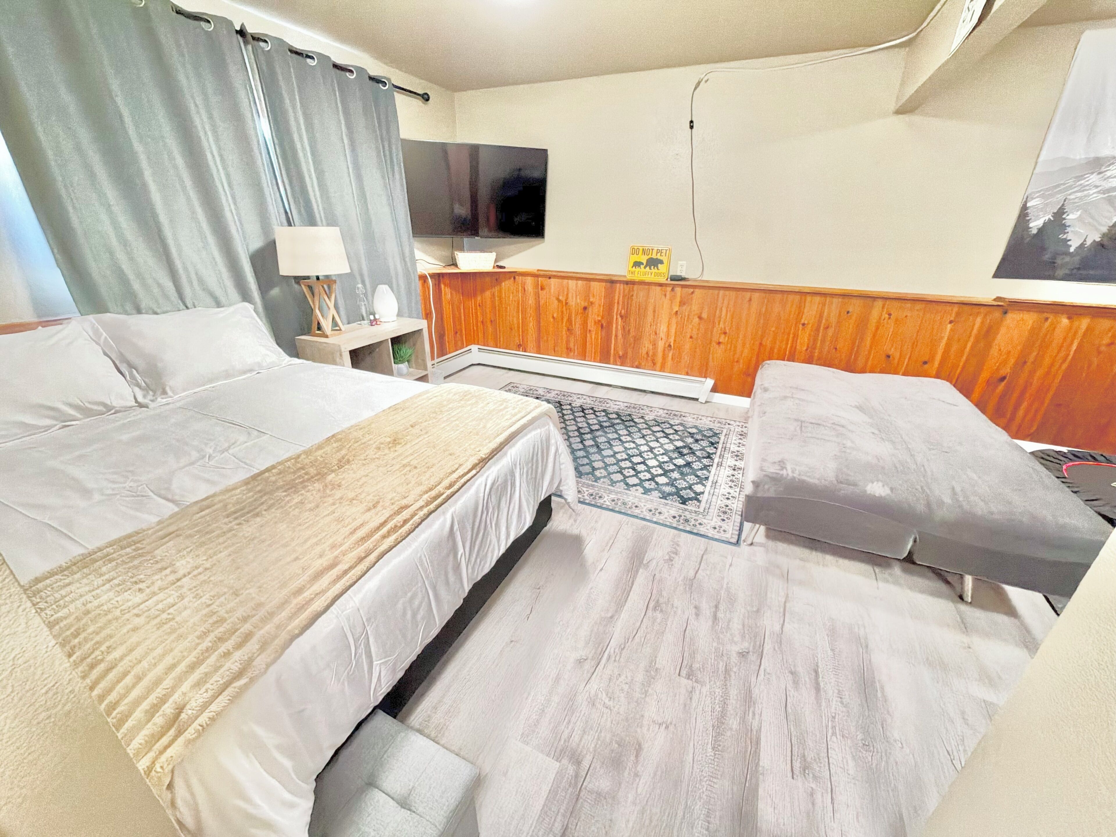 Una habitación de hotel con una cama, un televisor, un panel de pared de madera y una alfombra.