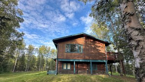 Une cabane en bois à deux étages, dotée d’un balcon et entourée d’une zone boisée.
