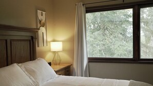 Un lit bien fait, avec une tête de lit en bois, une lampe de chevet et une fenêtre avec des rideaux.