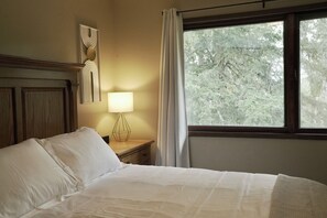 A neatly made bed with a wooden headboard, a bedside lamp, and a window with curtains. - 3BD/2BA Hideaway Cabin-Style Escape in the Heart of Alaska (Wasilla)