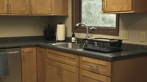 Une cuisine avec des meubles de rangement en bois, un évier en acier inoxydable et une fenêtre donnant sur les arbres.