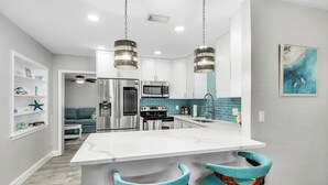 Een moderne keuken met een centraal kookeiland, roestvrijstalen apparatuur, accentmuren in teal en barstoelen.