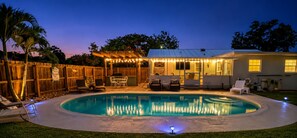 A backyard with a swimming pool, outdoor seating, and a covered patio area.