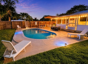 A backyard with a swimming pool, lounge chairs, and a covered patio area.
