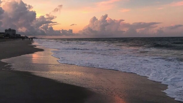 Een strand met golven die zachtjes op het strand komen, gebouwen op de achtergrond en een zonsonderganglucht.
