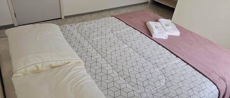 Una cama bien hecha con una colcha estampada y una toalla rosa sobre una mesita de noche.