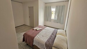 A bedroom with a bed, a door, and a window with curtains.