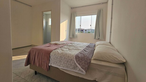 A bedroom with a bed, a window with curtains, and a view of buildings outside.